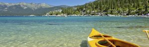 A yellow kayak sits on the beach in Lake Tahoe facing the water.