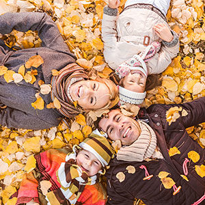 family of four laying on yellow autumn leaves smiling for picture