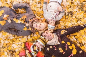 family of four laying on yellow autumn leaves smiling for picture