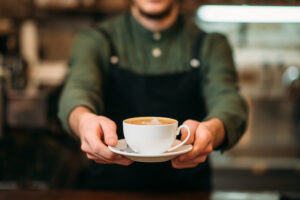 Waiter in black apron stretches a cup of coffee